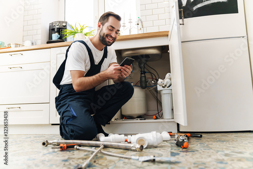 Man plumber work in uniform indoors using mobile phone. photo