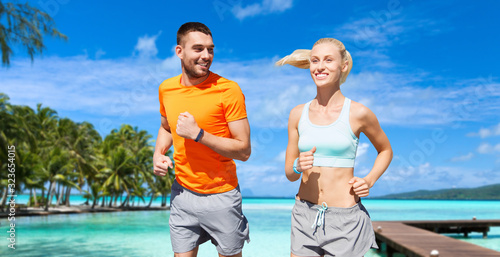 sport, healthy lifestyle and people concept - smiling couple with fitness trackers running at summer over city street on background