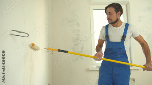 Repairman in uniform paints a wall in the flat