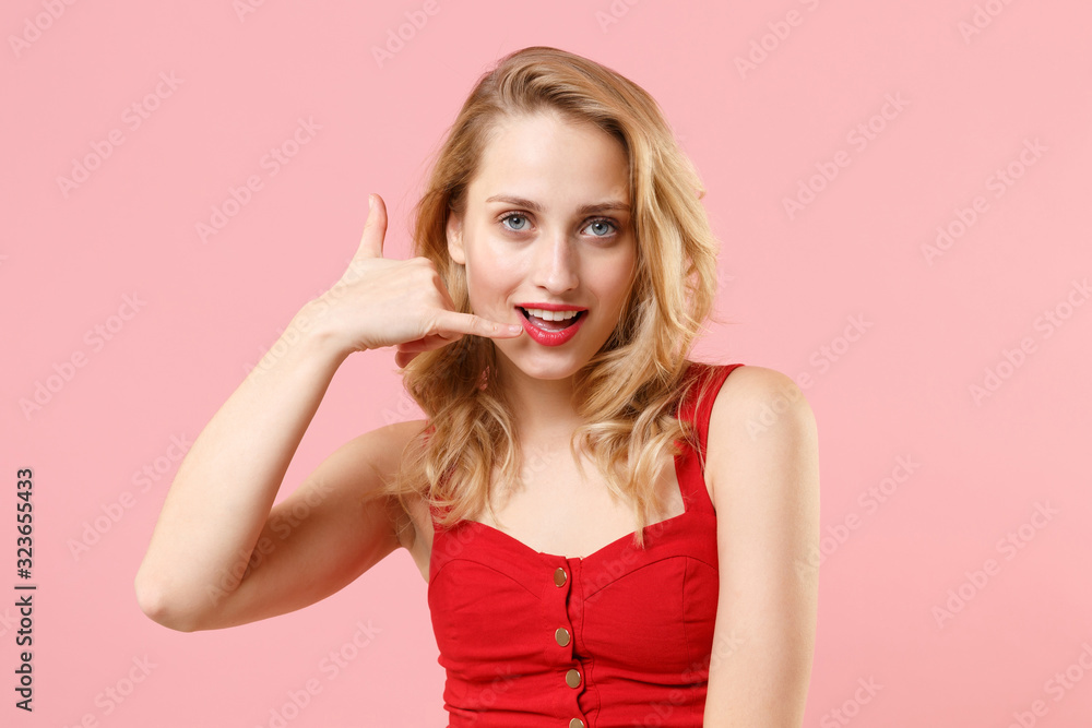 Beautiful young blonde woman girl in red sexy clothes posing isolated on pastel pink background studio portrait. People lifestyle concept. Mock up copy space. Doing phone gesture says call me back. Beautiful young blonde woman girl in red sexy clothes posing isolated on pastel pink background studio portrait. People lifestyle concept. Mock up copy space. Doing phone gesture says call me back.