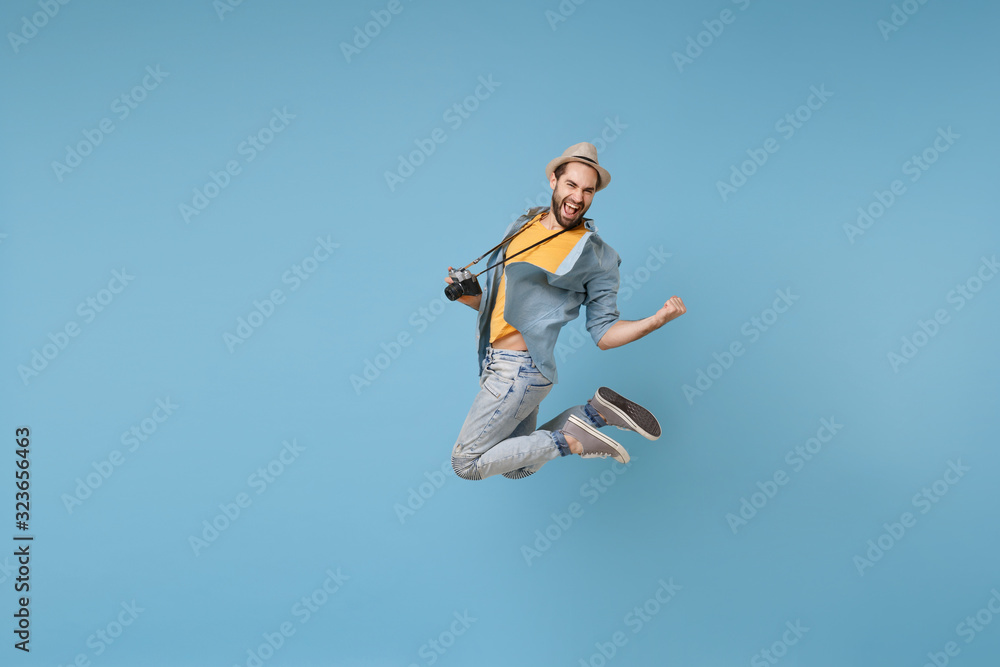 Joyful traveler tourist man in yellow casual clothes with photo camera isolated on blue background. Male passenger traveling abroad on weekend. Air flight journey concept Jumping doing winner gesture.