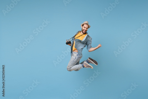 Joyful traveler tourist man in yellow casual clothes with photo camera isolated on blue background. Male passenger traveling abroad on weekend. Air flight journey concept Jumping doing winner gesture.