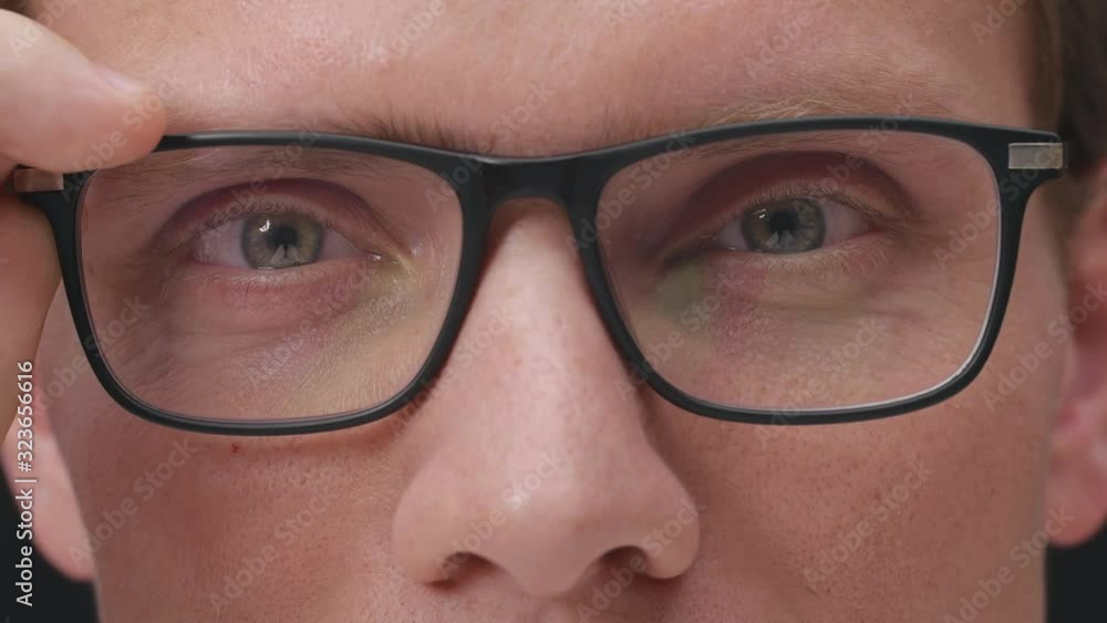 Macro of young man wearing eyeglasses winking isolated over black background Macro of young man wearing eyeglasses winking isolated over black background