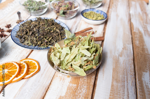 Dry linden leaves and flowers in plate as one of ingredients of herbal healthy green tea on wooden background