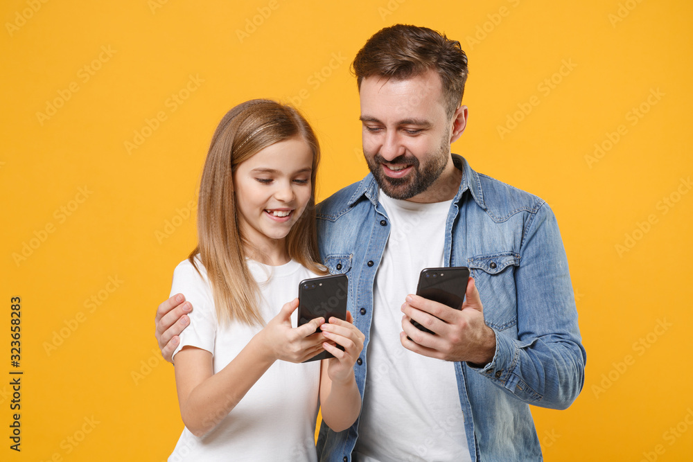 Smiling man in casual clothes with child baby girl. Father little kid daughter isolated on yellow background. Love family day parenthood childhood concept. Use mobile phone typing sms message hugging. Smiling man in casual clothes with child baby girl. Father little kid daughter isolated on yellow background. Love family day parenthood childhood concept. Use mobile phone typing sms message hugging.
