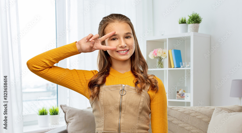 winning gesture, emotions and people concept - happy smiling young teenage girl showing peace hand sign home room background