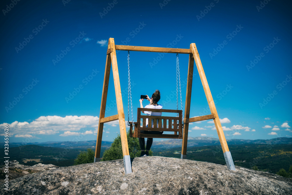 a woman takes a selfie while she is sitting on a wooden swing a woman takes a selfie while she is sitting on a wooden swing