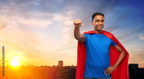 super power and people concept - indian man in red superhero cape making winning gesture over sunset in city background