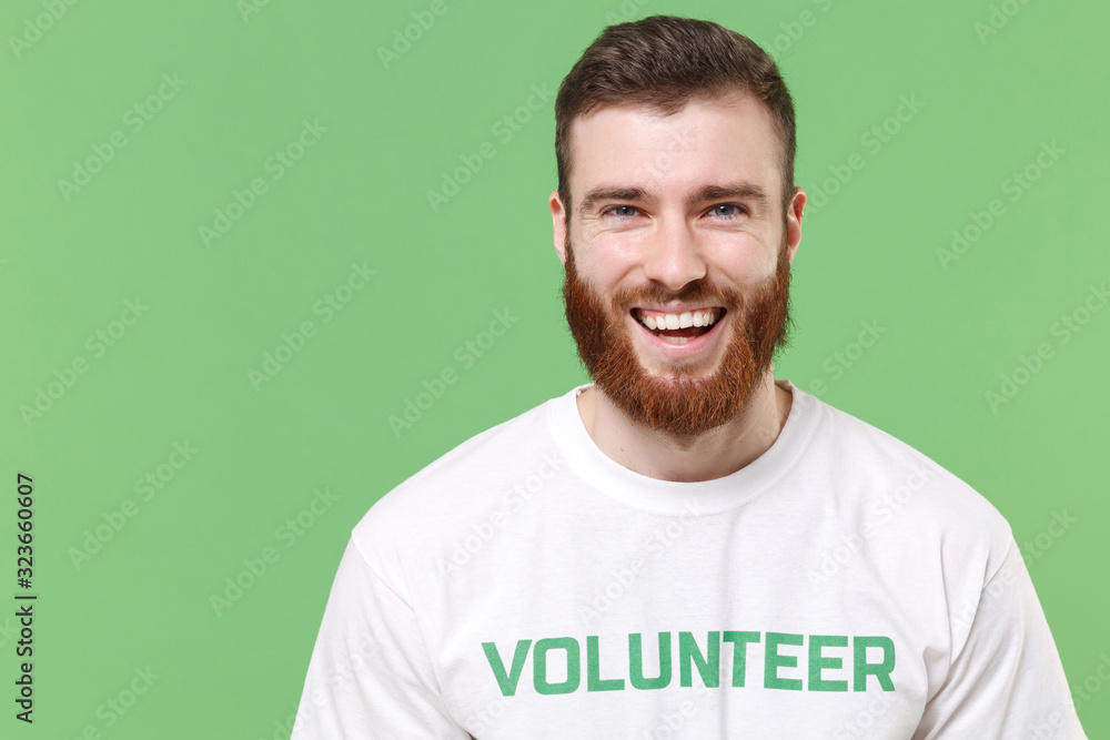 Laughing funny young bearded man in white volunteer t-shirt isolated on pastel green background studio portrait. Voluntary free work assistance help charity grace teamwork concept. Looking camera. Laughing funny young bearded man in white volunteer t-shirt isolated on pastel green background studio portrait. Voluntary free work assistance help charity grace teamwork concept. Looking camera.