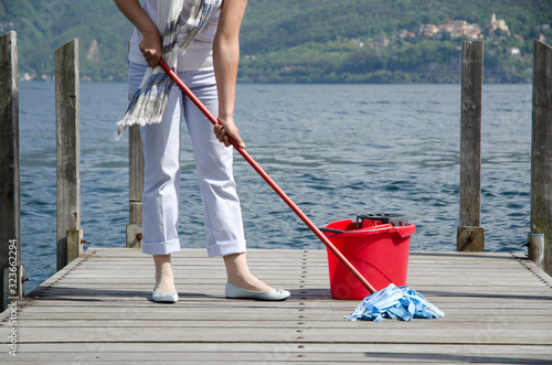 Woman Scrubs the Pier over the Alpine Lake with Cleaning Equipment in Switzerland. photo