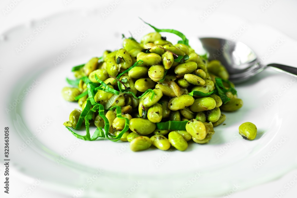 Boiled fava beans with spoon on white plate, close-up. Boiled fava beans with spoon on white plate, close-up.