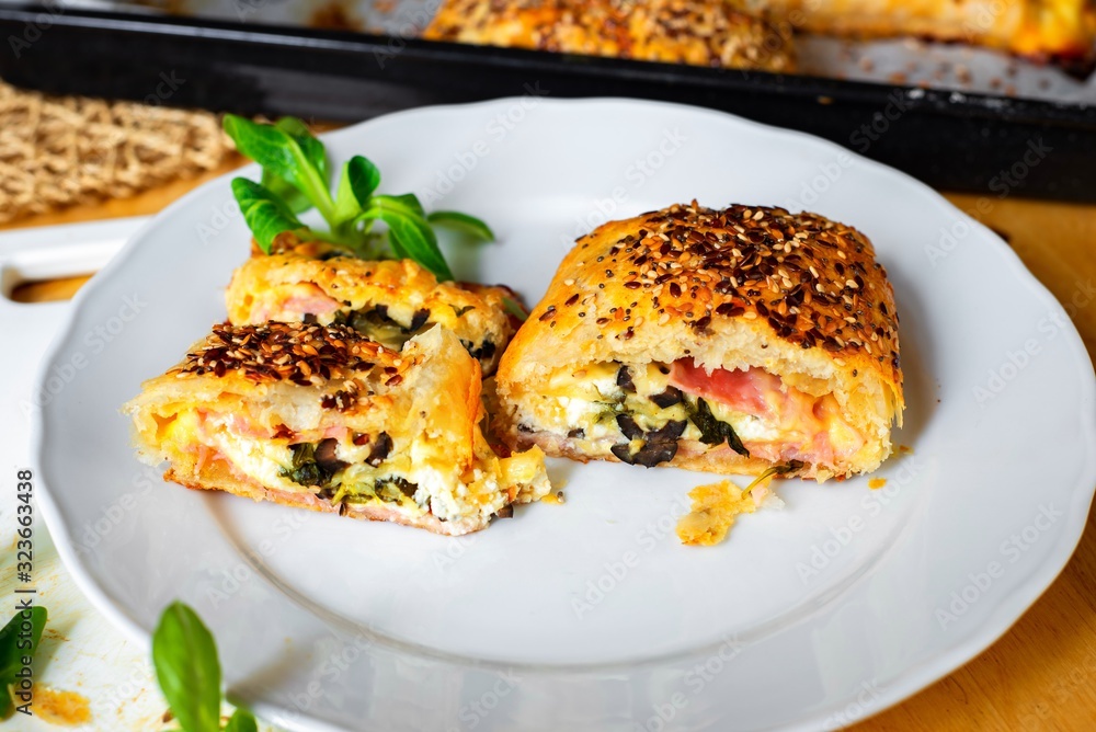 Sliced baked puff pastry bun with ham, cheese and olive on plate and on baking tray. Sliced baked puff pastry bun with ham, cheese and olive on plate and on baking tray.