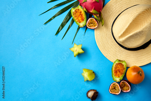 summer holidays  vacation and travel concept - close up of straw hat and exotic fruits on blue background