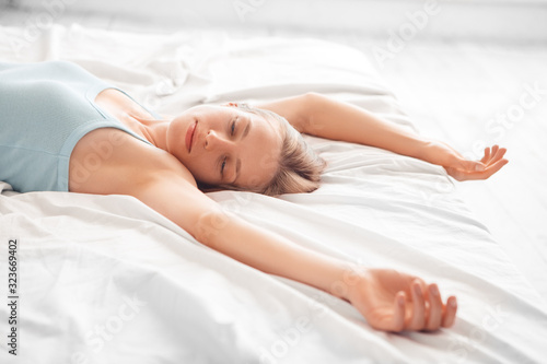 Morning at Home. Woman lying on bed hands aside smiling sleepy close-up