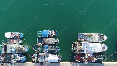 Aerial top down view of old Italian fishing harbor showing several docked trawlers waiting for sailing out beautiful colorful scene with azure blue ocean water and multi colored wooden ships 4k photo