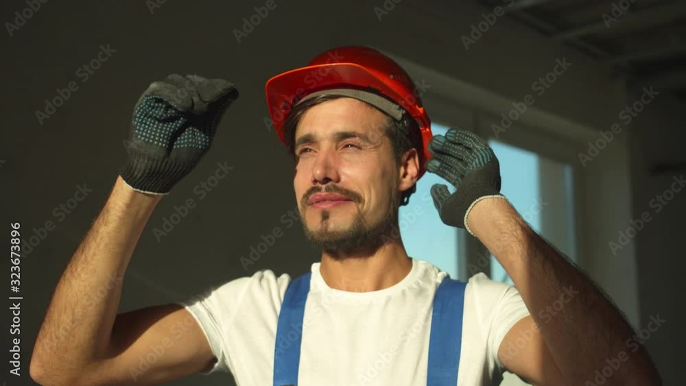 Slow motion, smiling builder stands and puts on protective helmet Slow motion, smiling builder stands and puts on protective helmet
