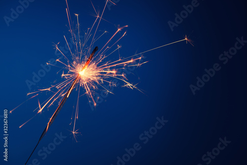 Party sparkler burning bright with sparks on blue background with copy-space.
