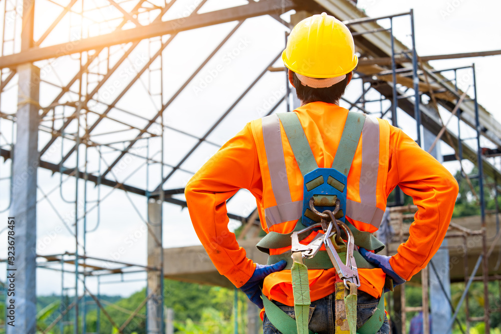 Construction worker wearing safety harness and excavator wearing orange  reflective vest standing in front at construction site. Stock Photo