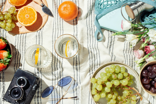 Feminine summer picnic flatlay, fruits, berries and lemon water on striped cotton blanket