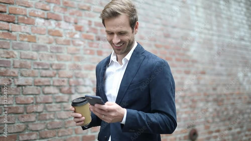 young smart casual man drinking his coffee while reading interesting news on his phone young smart casual man drinking his coffee while reading interesting news on his phone