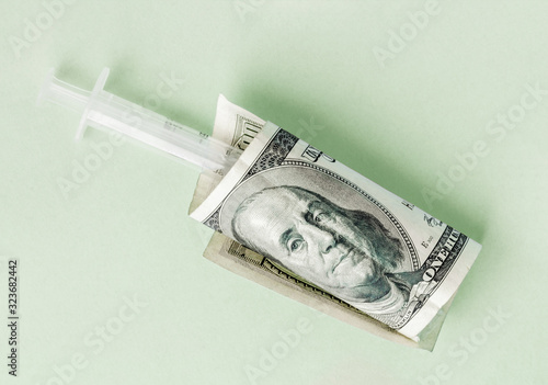 Syringe is wrapped in a hundred-dollar bill, the concept of addiction and addiction, the high cost of medical vaccines, a flat lay with a green background, virus vaccination