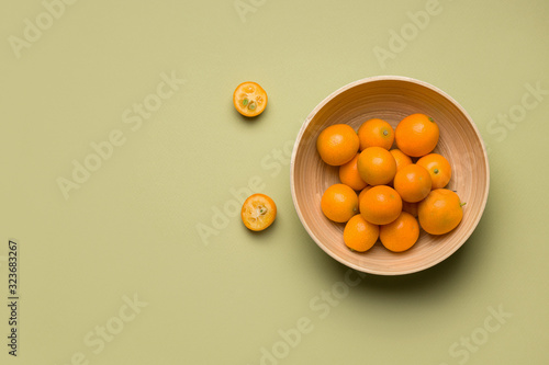 tropical citrus kumquat fruit in a bamboo bowl on a green background. copy space