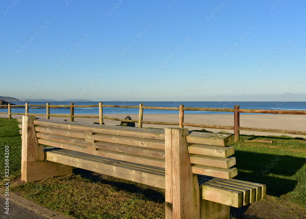 Wooden bench on a beach promenade with morning light and blue sky. Arteixo, Coruña, Galicia, Spain.