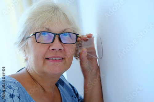 A woman uses a glass cup to listen to neighbors through the wall photo