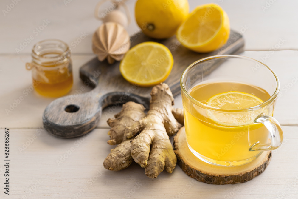 Ginger tea on lemon on glass mug on light wooden background for help relieve cold and flu symptoms. Ginger tea on lemon on glass mug on light wooden background for help relieve cold and flu symptoms.