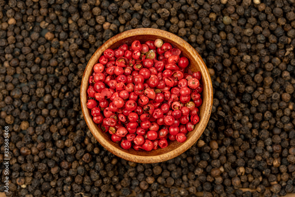 Spice background, Background made of many whole black peppercorns and a wooden bowls filled with red peppercorns , extreme close up, top view Spice background, Background made of many whole black peppercorns and a wooden bowls filled with red peppercorns , extreme close up, top view