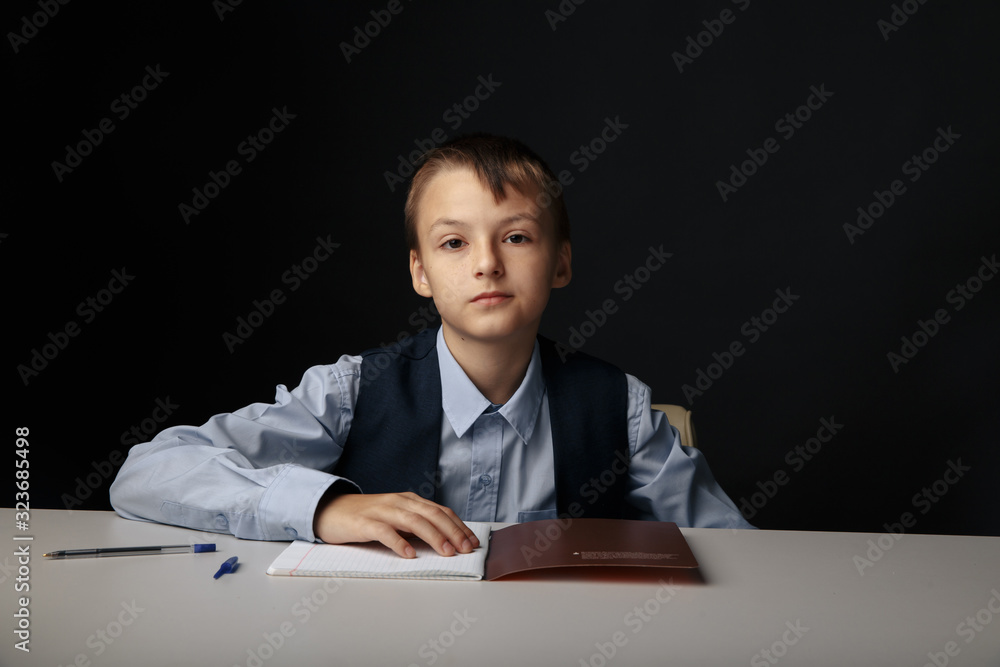Education at school concept. Boy sitting at the table and studying isolated in the grey classroom Education at school concept. Boy sitting at the table and studying isolated in the grey classroom