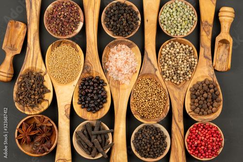 Spice and Food - Background made of many various spices and pepper varieties in small wooden bowls and cooking spoons made of olive wood on a black background