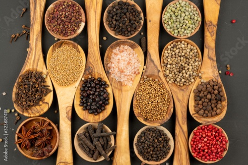 Spice and Food - Background made of many various spices and pepper varieties in small wooden bowls and cooking spoons made of olive wood on a black background