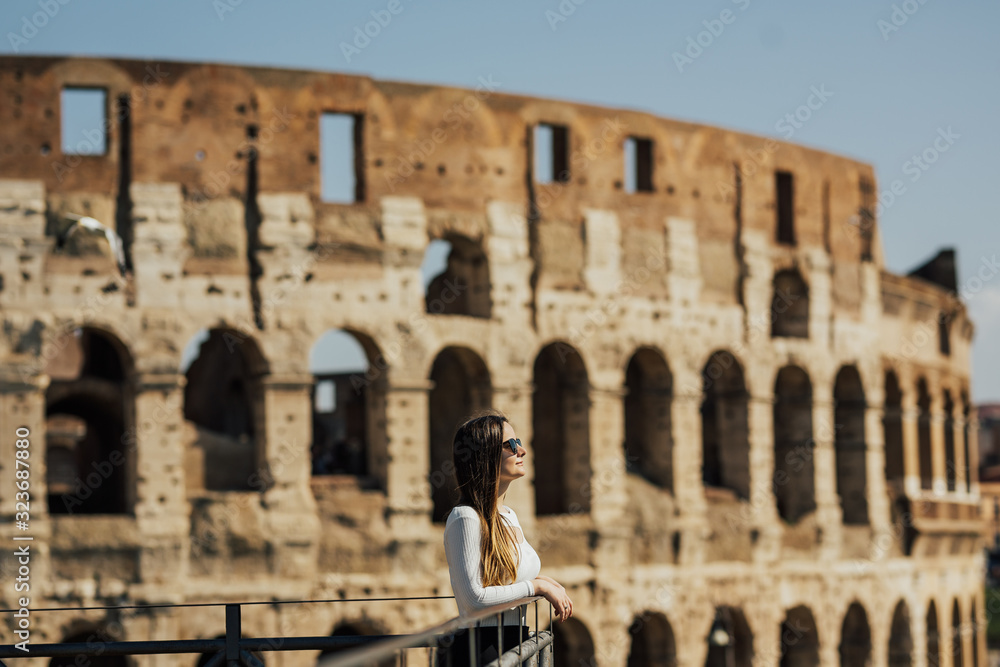 Beautiful woman in romantic dress standing near Coliseum, Rome, Italy. Young woman enjoy Italian vacation in Europe. Traveling through the coliseum photo of a girl traveler.