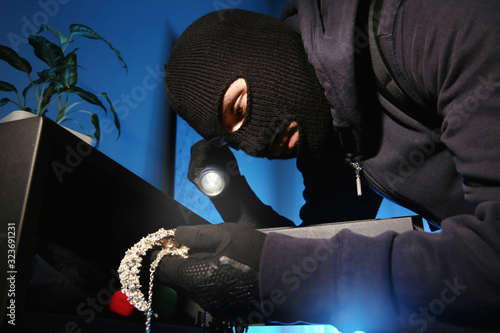 Thief taking jewelry out of steel safe indoors at night photo