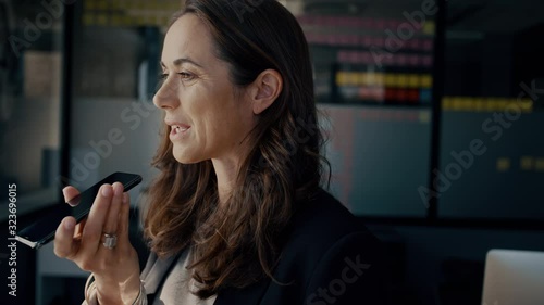 Mature businesswoman speaking into her cell phone. Business professional talking over speakerphone while standing in the office.