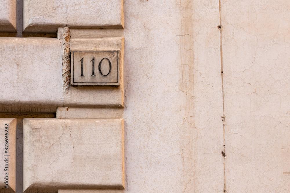 number 110, ancient house number plate on brick wall, Italy