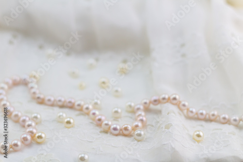 Pearl necklace on lace dress background - selective focus on pink and champagne pearls