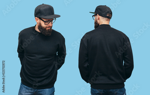 Handsome hipster guy with beard wearing black blank hoody or sweatshirt from front and back and black cap with space for your logo or design on blue background. Mockup for print photo