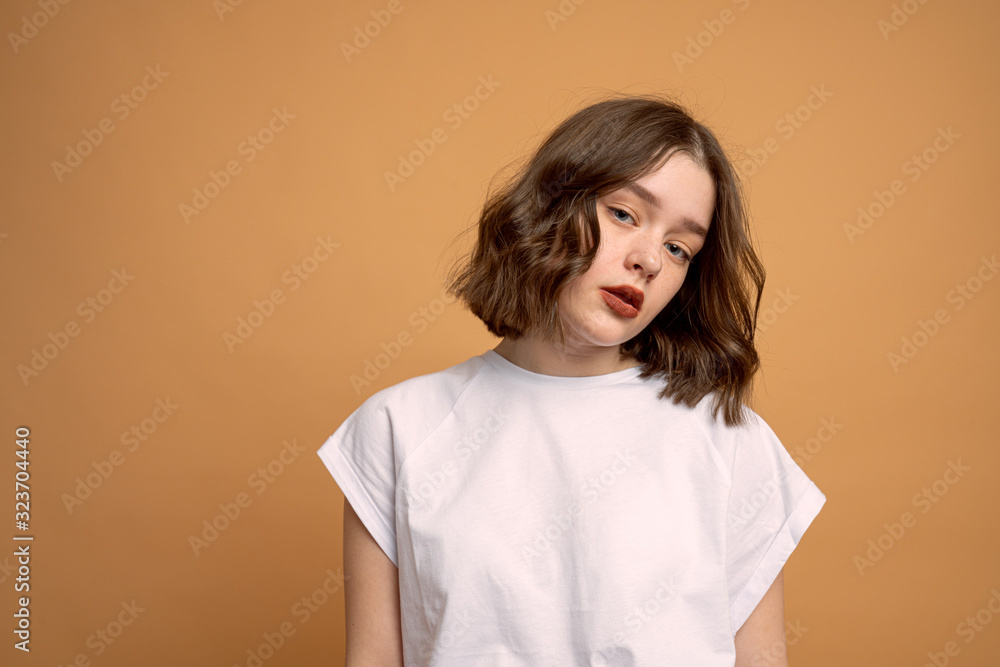 Confident curly girl in white t-shirt looking at the camera against orange background Confident curly girl in white t-shirt looking at the camera against orange background