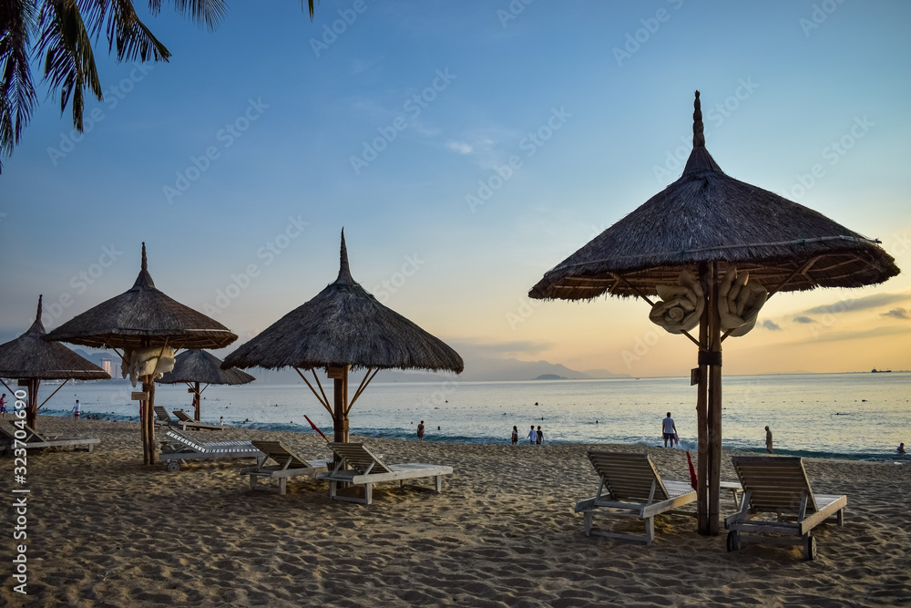 Straw umbrellas on a sandy beach at dawn and wooden deck chairs by the sea