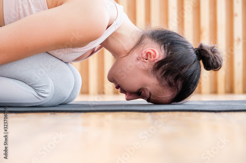 Close-up of young calm meditating woman doing pose of child balasana lying on rug on floor during home workout. Concept of lovers of yoga and meditation. Advertising space