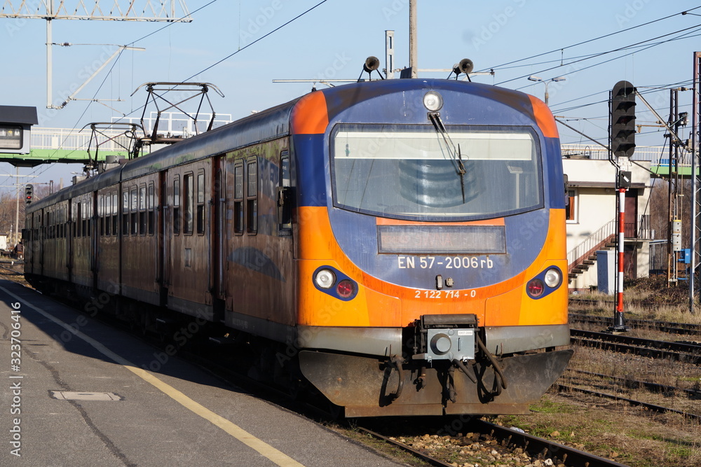 The orange and blue electric train at the railway station. Track, poles and supports for current-carrying lines.