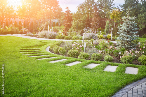 Landscaping. Lawn with green grass and flowers on a flowerbed in the sun. Copyspace.