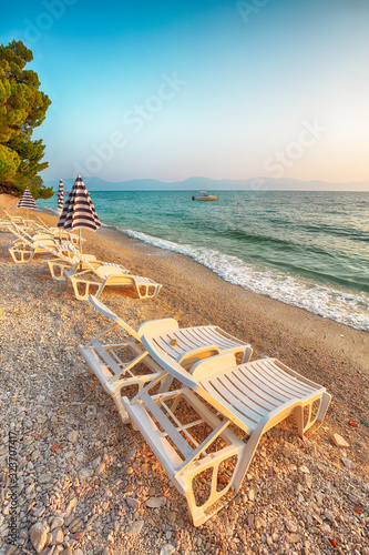 Fototapeta Naklejka Na Ścianę i Meble -  Sun loungers and beach umbrellas at sunset on the beach of Gradac in Makarska riviera