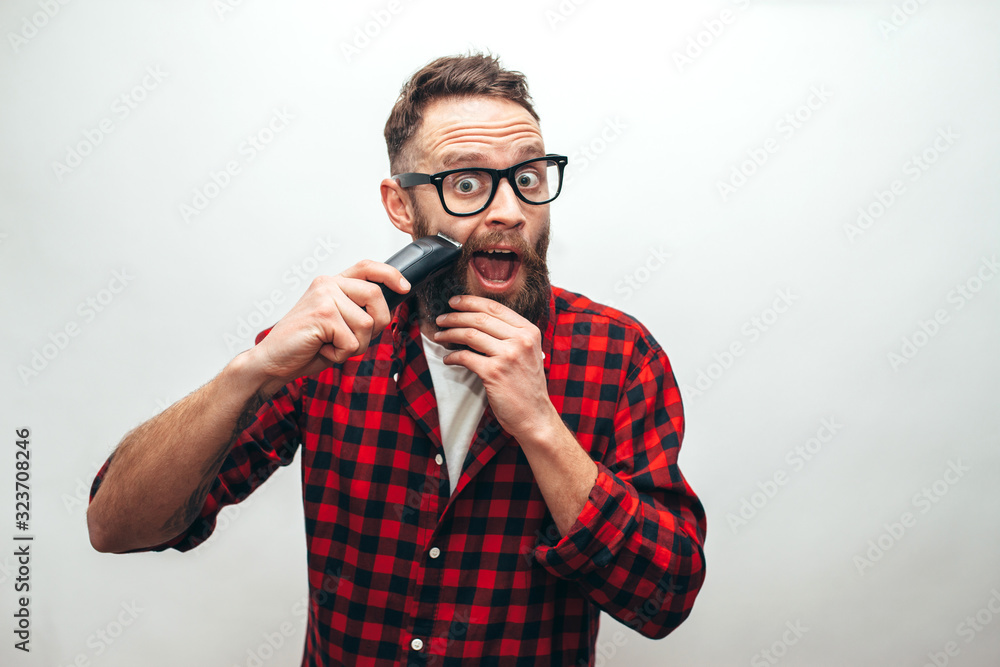 Handsome man shaving beard with an electric razor isolated over gray background Handsome man shaving beard with an electric razor isolated over gray background