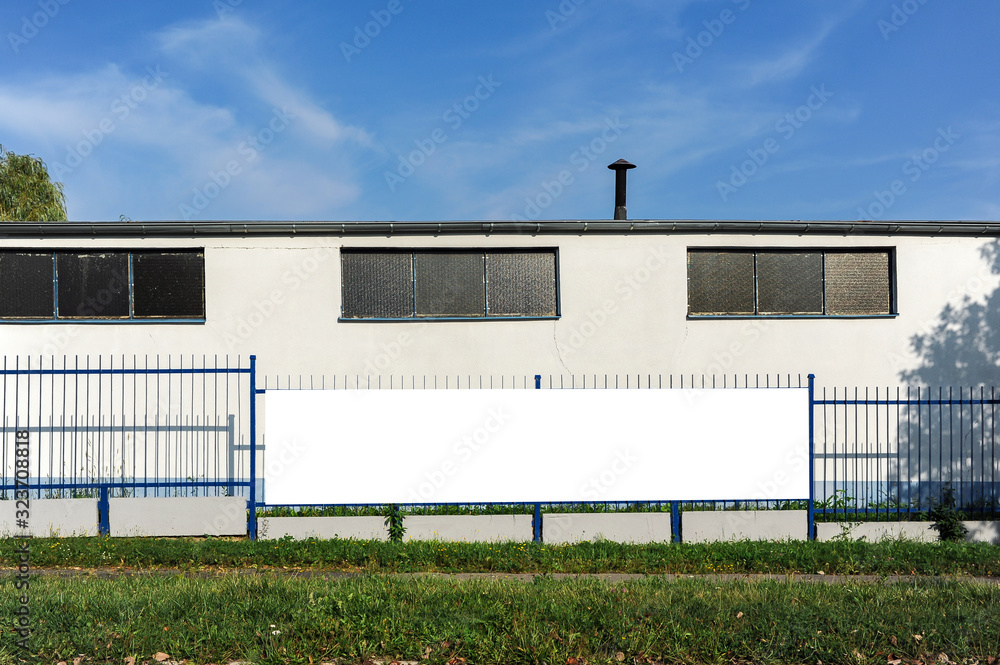 Blank white advertising banner mounted on the fence of industrial building