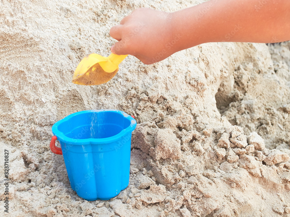 Hand of child playing in the sandbox with yellow scoop and blue bucket Hand of child playing in the sandbox with yellow scoop and blue bucket