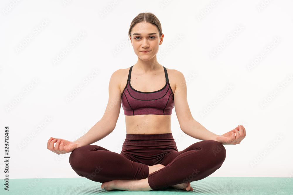 Portrait of a calm european fitness woman resting while sitting and meditating isolated over white background