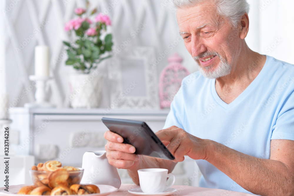 Senior man using tablet while drinking tea at home Senior man using tablet while drinking tea at home